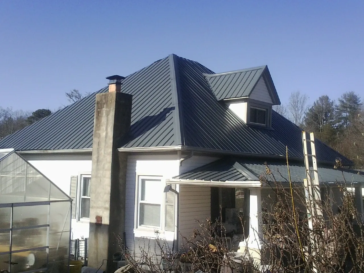 Dark blue standing seam metal roof on a white farmhouse with dormer — Slate & Tile Roof Repair by Roofing Brothers in Southlake