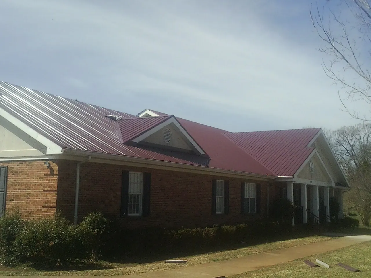 Red metal roof with gabled entries on a long brick building, from a Hail Damage Roof Repair job in Southlake