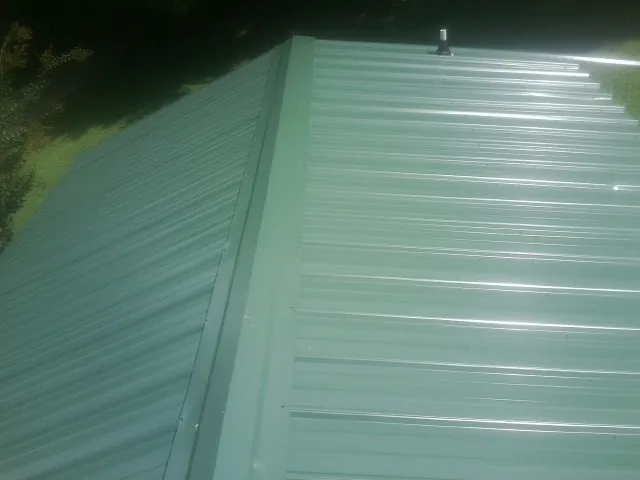 New green metal panels meeting at the ridge of a roof — Flat Roof Repair work by our crew in Southlake