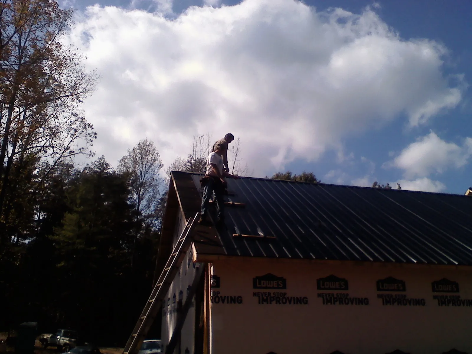 Roofer fastening dark metal panels high against a cloudy sky, from a Roof Inspection job in Southlake