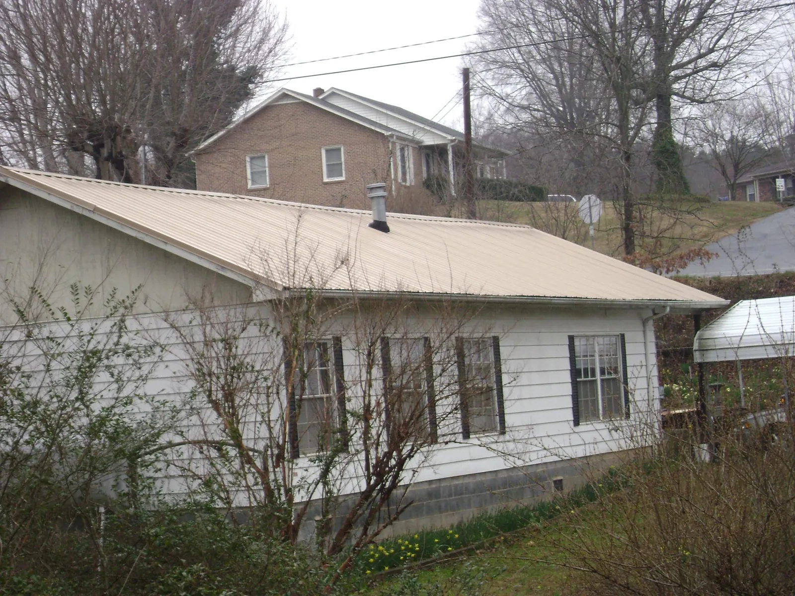Tan metal roof on a white sided house set into a hillside — Commercial Roofing by Roofing Brothers in Southlake
